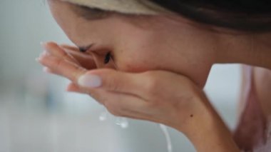 Evde temizlikçi kadın var. Yakın çekim. Sabah hijyen rutininden zevk alan tatmin olmuş bir kadın. Rahatlamış bir kız banyo lavabosunun görüş alanında cildine su sıçratıyor. Ev kaplıcası ve refah