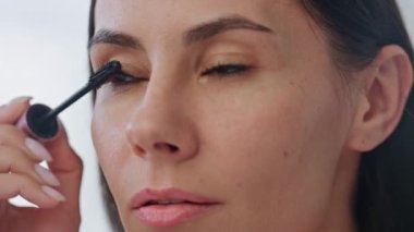 Kapalı mekanda rimel süren ciddi bir model. Odaklanmış kadın yüzü aynada fırçayı tek başına tutuyor. Makyaj hazırlayan kendine güvenen güzel bir kadın beyaz banyo odasına makyaj malzemesi koyuyor.