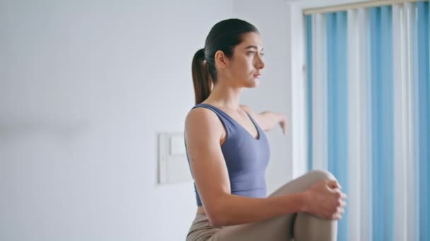 瘦小的女孩抱着膝盖在家里伸展着 肌肉发达的女人正在热身 准备在家里早上锻炼 迷人的苗条身材的女士单腿站在公寓锻炼 体育概念 — 图库视频影像