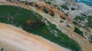 İnsansız hava aracı kumlu yamaçları çekti. Doğa yakın plan. Hava manzaralı tepeler alçak yeşil bitkileri kapsıyordu. Kasvetli gri gökyüzü altında beyaz köpüklü okyanus sörfü yavaş çekim. Deniz yüzeyi dramatik bulutlu hava