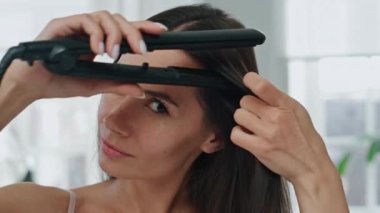 Esmer kadın banyo odasındaki portrede saçlarını düzeltiyor. Evde demir teçhizat kullanarak gülümseyen bir model. Uzun Chevelure Pov 'da kamera tasarımı yapan tımar edilmiş kadın. Sabah rutin saç bakım konsepti