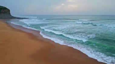 Kasvetli okyanus kumsalı manzaralı hava manzarası. Beyaz köpüklü deniz dalgaları altın sahil şeridinde ağır çekimde akıyor. Temiz kıyı şeridi derin fırtınalı deniz sörfü ile buluşuyor. Manzaralı güzel panoramik doğa konsepti