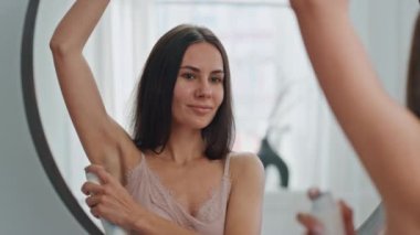 Gülümseyen kadın evde terleme önleyici uyguluyor. Koltuk altlarına deodorant sıkan hoş bir bayan günlük işlemlerin tadını çıkarıyor. Mutlu kız ayna yansıması. Vücut bakımı günlük hijyen rutini kavramı 