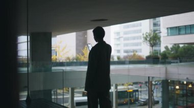 Şehir manzarasında cep telefonu kullanan bir kadın silueti. Rahat iş kadını Scrroll haberleri sosyal medya karanlık ofis balkonunda yürüyor. Bilinmeyen çalışan akıllı telefonu tutarak ara verdi. Kurumsal insan kavramı