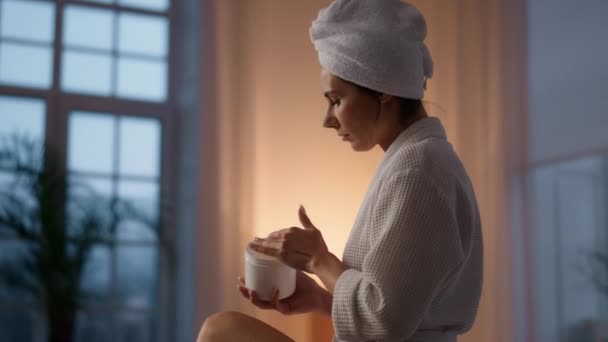 漂亮的女人在浴室的特写镜头里给腿保湿 白袍女士在干性皮肤上涂了补液 头部毛巾模型把奶油放在夜间蜡烛内部 Skincare Spa概念 — 图库视频影像