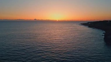 Gün batımında dalgalanan deniz sahili hava manzarası. Karanlık ve dingin okyanus yüzeyinde altın şafak. Gün batımında ağır çekimde hareket eden huzurlu dalgalar. Meditasyon yapan sakin deniz manzarası