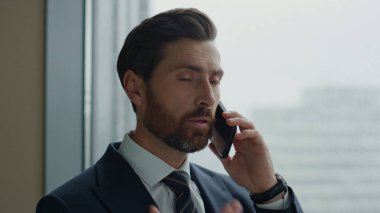 Mali danışman ofisin panoramik penceresinde telefonla konuşuyor. Modern akıllı telefonu kullanarak müşteri danışmanlığı. Kendine güvenen sakallı iş adamı telefon görüşmesi yapar..