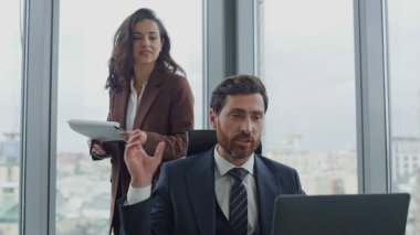 Çekici kadın asistan, CEO 'nun belgeleri okumasına yardım ediyor. Lüks şirket ofisinde birlikte çalışan kendine güvenen iki iş arkadaşı. Yönetici dizüstü bilgisayarla oturuyor.