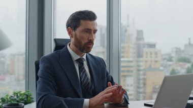 Yakışıklı sakallı yönetici, bilgisayardaki internet aramasını kullanarak ofis masasını kapatıyor. Kendine güvenen iş adamı el sallayarak video konferansını bitiriyor. Başarılı patron web kamerasında konuşuyor..