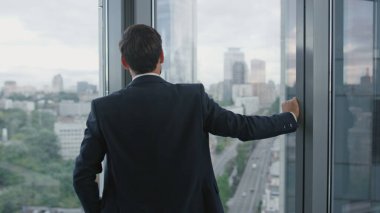 Ciddi sakallı bir iş adamı panoramik pencerenin yanında duran şirket stratejisini düşünüyor. Düşünceli yönetici mali sorunlar için el ele tutuşuyor. Ofis çalışanının portresi.