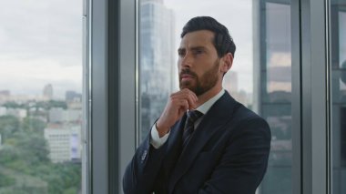 Şehir manzarasına bakan düşünceli genel müdür ofis penceresinin yanında duruyor. Kendine güvenen sakallı iş adamı şirket gelişimini düşünüyor iş sorunları yaratıcı fikirler kariyer büyümesi.