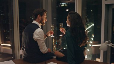 Çalışma masasında oturmuş şampanya içen iki meslektaşım panoramik pencereden şehrin muhteşem manzarasını izliyorlar. Mutlu iş arkadaşları başarılı bir iş gününden sonra dinleniyor. Projeyi birlikte kazanacağız..