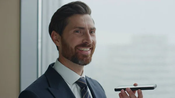 Smiling attractive manager finishing telephone talk satisfied by success working negotiation close up. Happy bearded business man holding modern smartphone using gadget for professional communicating.