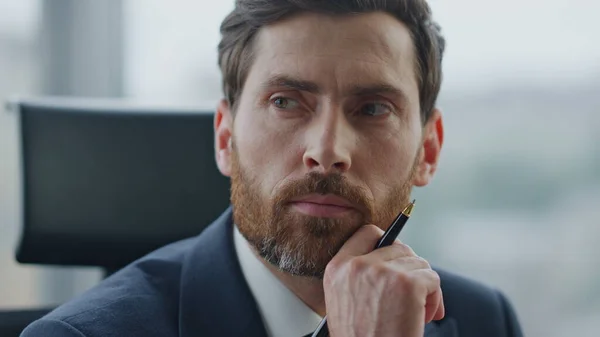 Portrait of thoughtful boss working alone in modern office wearing elegant suit. Attractive bearded businessman thinking about business strategy company problems. Manager reading documents close up.