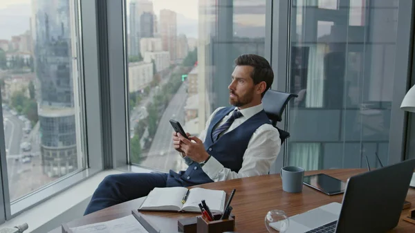 Empresario Serio Sosteniendo Teléfono Inteligente Sentado Oficina Cerca Ventana Panorámica —  Fotos de Stock