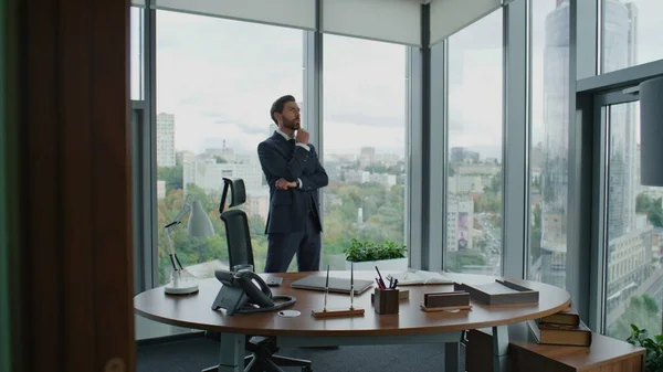 Serious top manager waiting meeting walking around at modern office with panoramic windows. Confident bearded businessman looking at wristwatch checking time. Employee thinking about work day ending.