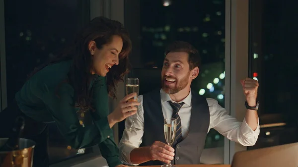 两位年轻的成功伴侣欢欣鼓舞在现代办公室的深夜喝香槟取得的商业成就 与有魅力的女商人一起庆祝成功的生意人 — 图库照片