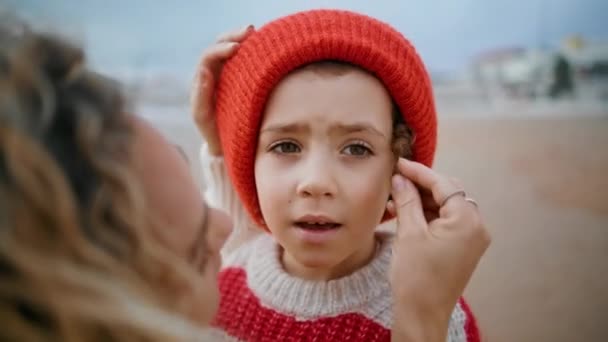 可爱的男孩休息秋天的海滩与妈妈的特写 有爱心的母亲在户外周末帮你戴礼帽 表达爱心 可爱的卷曲的孩子在海滨戴着温暖的针织帽子 养育子女的概念 — 图库视频影像