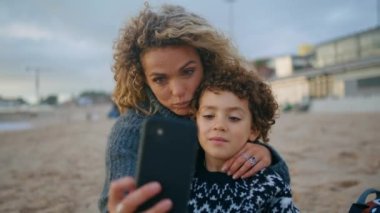 Sonbahar kumsalında komik selfie çeken bir aile. Mutlu anne oğul dışarıda piknik yaparken eğleniyor. Neşeli bebek bakıcısı, bekâr anne telefonu tutuyor. Aşk ilişkileri konsepti. 