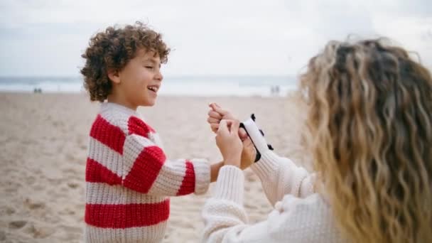 妈妈帮助在海滩特写上放风筝 笑笑可爱的儿子牵着线在外面玩玩具 年轻的保姆教孩子如何共度美好时光 无忧无虑的童年概念 — 图库视频影像