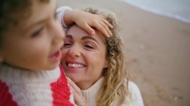 Okyanus kıyısında çocuğu kucaklayan bir anne. Gülümseyen bir kadın, aşık bir çocuğa bakıyor ve sonbahar haftasonunun tadını çıkarıyor. Güzel bir ebeveyn deniz kenarında yakışıklı bir çocukla tatil yapıyor. Anneler Günü konsepti