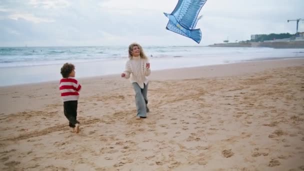 孩子们和妈妈一起在多风的海滩放风筝 兴奋的母亲在家庭周末帮儿子和可爱的男孩玩耍 支持父母一起玩儿童游戏 爱的关系概念 — 图库视频影像
