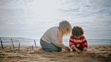 Anne, küçük oğluyla sonbahar kumsalında dinleniyor. Kaygısız aile okyanus kıyısında kumdan kale inşa ediyor. Kıvırcık, bekar anne dadı çocukla iyi vakit geçiriyor. Aile oyunları yaratıcılığı.