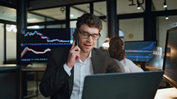投資グラフでスマートフォンを話しているビジネスマンの笑顔 オフィスの株式市場戦略についての遅いコンサルティングクライアントで働く成功したセールスマン フレンドリーなトレーダープロの呼び出しルックコンピュータ — ストック動画