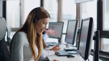 Gülümseyen operatör veri merkezinde bilgisayarı daktilo ediyor. İşteki neşeli kadın asistan. Müşteriye uzaktan bağlanan olumlu müşteri desteği profesyonel internet taraması. Kulaklıklı mutlu ofis yöneticisi