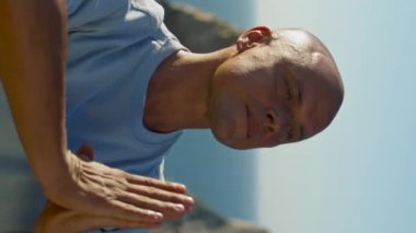 Yoga yapan bir sporcu okyanus manzarası. Odaklanmış bir adam güzel bir uçurumun kenarında namaste pozisyonunda meditasyon yapıyor. Kel adam güneş ışığında dinlenme egzersizi yapıyor. Farkındalık konsantrasyonu.