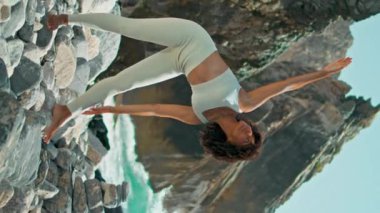 Güzel kayalık plajda utthita trikonasana egzersizi yapan dikey sakin kadın. Afrika kökenli Amerikalı rahat kız güneşli bir günde okyanus dalgalarının önünde yoga pozu veriyor. Sıska sporcu kadın, dışarıda uzanıyor.