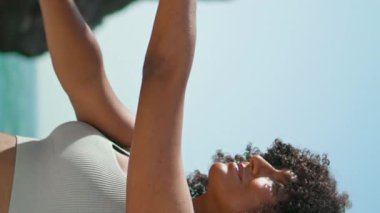 Huzurlu bir yogi kızı, Ursa sahilinin dikey manzarasında el ele tutuşup esneme egzersizleri yapıyor. Gülümseyen Afro-Amerikan sporcu kadın yoga pozu veriyor. Sağlıklı vücut eğitimi alan kadın