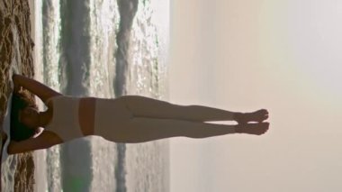 Dikey Afro-Amerikalı kadın gün doğumunda deniz kıyısında yoga pozu veriyor. Atletik kız vücut dengesi üzerinde duruyor. Ursa sahilinde yaz akşamı Asana antrenmanı yapan güçlü bir sporcu kadın.