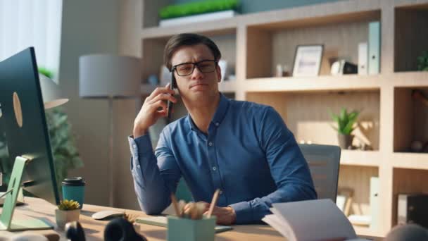 真剣に起業家はオフィスで携帯電話を話している 現代的なインテリアでスマートフォンの呼び出しを持つ成功したビジネスマンを閉じます コンピュータテーブルキャビネットに座って電話をかける眼鏡管理者 — ストック動画