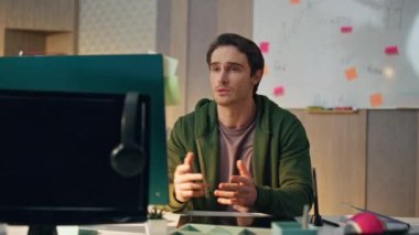 İş yerindeki video ekranında gevşemiş uzman selamlama bilgisayarı. Kapalı mekanda el sallayan yetenekli adam. Kendine güvenen tasarımcı sanal sohbette açıklayan bir defter açıyor