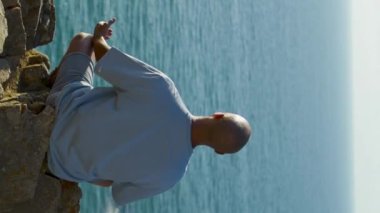 Yogacı adam güneş ışığında uçurumun kenarında meditasyon yapıyor. Nilüfer pozisyonunda nefes alan bilinmeyen atletik kel adam.