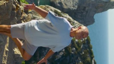 Yogacı adam yazın okyanus kayalıklarında Asana egzersizi yapıyor. Odaklanmış adam, dışarıda güneş ışığında namaste jesti yapıyor. Rahatlamış sporcu doğa üzerine dikey video egzersizi yapıyor. Uyum meditasyonu