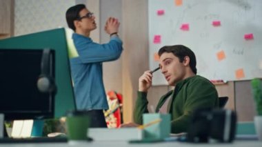 Yeni başlayanlar ofiste yakın planda konuşuyorlar. Gözlüklü adam top fırlatıyor, ortağı bilgisayar işyerinde omuz silkiyor. Kabinede yaratıcı kriz yaratan fikirleri araştıran iki meslektaş