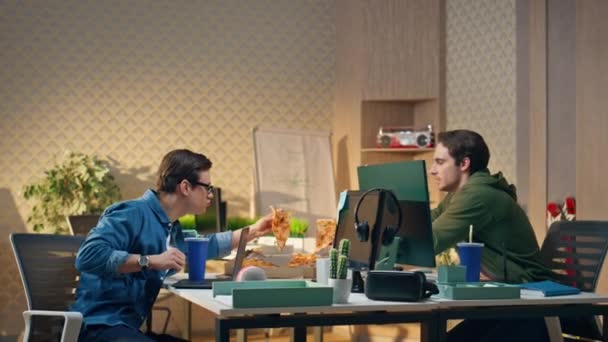 ハンガリーのスタートアップは 職場でピザのスライスをする おいしいおやつを一緒に楽しんでいる2人の若者 フレンドリーな男性同僚がオフィスで食品配送サービスを使用して企業ランチを共有 — ストック動画