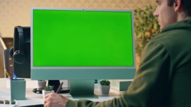 Odaklanmış sanatçı, güneşli iş yerinde tablet yaratarak yeşil ekrana bakıyor. Kromakey monitöründe çalışan ciddi bir yaratıcı. Yaratıcı tasarımcı kabinede grafik tabanlı bilgisayar çiziyor
