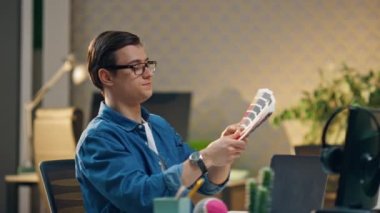 Genç yaratıcı ofiste renk örnekleri öneriyor. Bilgisayar masasında beyin fırtınası yapan tasarım uzmanları. Masada duran gözlüklü adam meslektaşına numuneleri gösteriyor. Tasarımcı seçim yapıyor