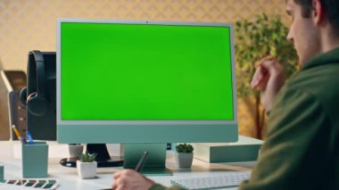 Tasarımcı ofiste Chromakey bilgisayar çizim tabletinde çalışıyor. Masa başında Stylus kalem tutan yeşil ekran bilgisayar aygıtı kullanan odaklanmış yaratıcı adam. Ciddi acemi bakışlı maket monitörü