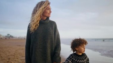 Rahat anne oğlu okyanus kıyısında yürüyor. Mutlu aile hafta sonları birlikte. Güzel anne baba sonbahar tatilinin tadını çıkarıyor. Sevimli çocuk annesinin elini tutarak dalgaları izliyor. Boş zaman yolculuğu konsepti