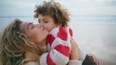 Mutlu anne, okyanus kıyısında oğlunu kucaklıyor. Samimi aile duyguları. Güzel kadın anne gözlerini kapatıyor dışarıda yakışıklı çocuğa sarılıyor. Sevimli kıvırcık çocuk ebeveynini öpüyor. Güzel anneler günü