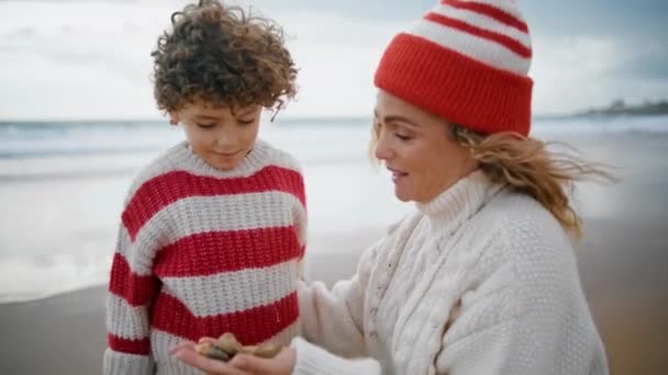 有爱心的母亲在海滩特写上亲吻孩子 秋天海滨周末 卷曲的小儿子抱着妈妈 单身妈妈教孩子一起享受假期 父母之爱支助概念 — 图库视频影像