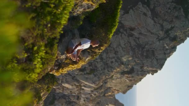 宁静的人沉思着大海的景色 平静的男人在悬崖边练习瑜伽在阳光的垂直视频 以运动为重点的运动员在令人叹为观止的景观中放松运动莲花的位置 禅样的生活方式 — 图库视频影像