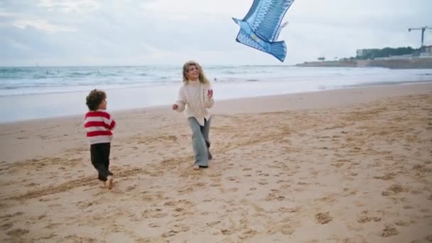 子供は風の強いビーチでお母さんとカイトを起動しようとします 家族の週末にかわいい男の子と遊ぶ息子を助ける興奮した母親 一緒に子供ゲームを楽しむ支援親 恋愛関係の概念 — ストック動画