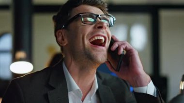 Gülümseyen proje yöneticisi yakın çekimde konuşuyor. Mutlu başarılı simsar iş yerinde cep telefonuyla konuşmanın tadını çıkarıyor. Neşeli adam borsa kârını tartışıyor.