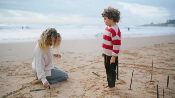 在多风的日子里 妈妈的孩子在海滨休息 美丽的家庭绘画海滩沙滩享受秋天的假期 可爱的卷曲的儿子说话的父母看着海浪来了 海滨欢乐的假期 — 图库视频影像