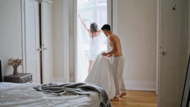 爱情对早上在卧室的例行公事 温文尔雅半裸的男人抱着毛毯在舒适的房间里 布鲁内特女人拉起窗帘看着窗户 懒惰的女朋友开始和男朋友共度美好的周末 — 图库视频影像